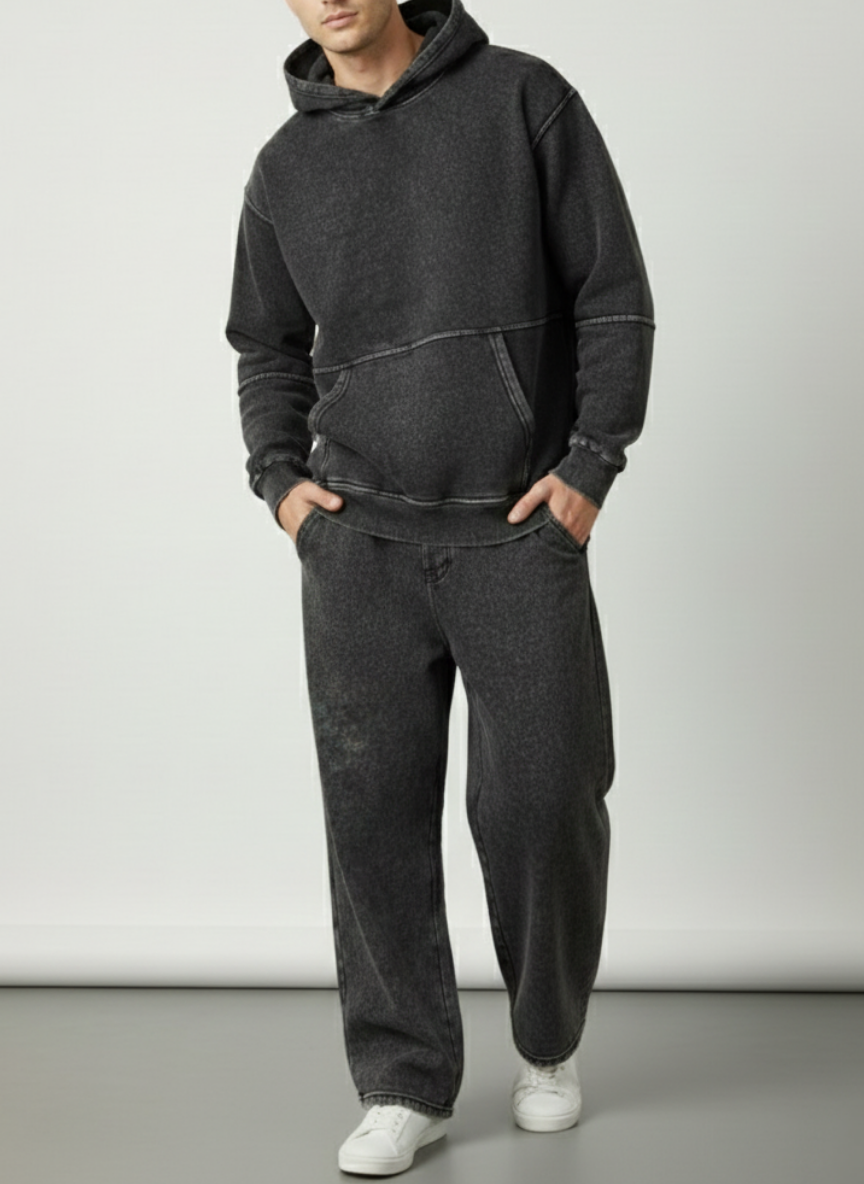 Person wearing a dark gray hoodie and pants with white shoes on a light gray background