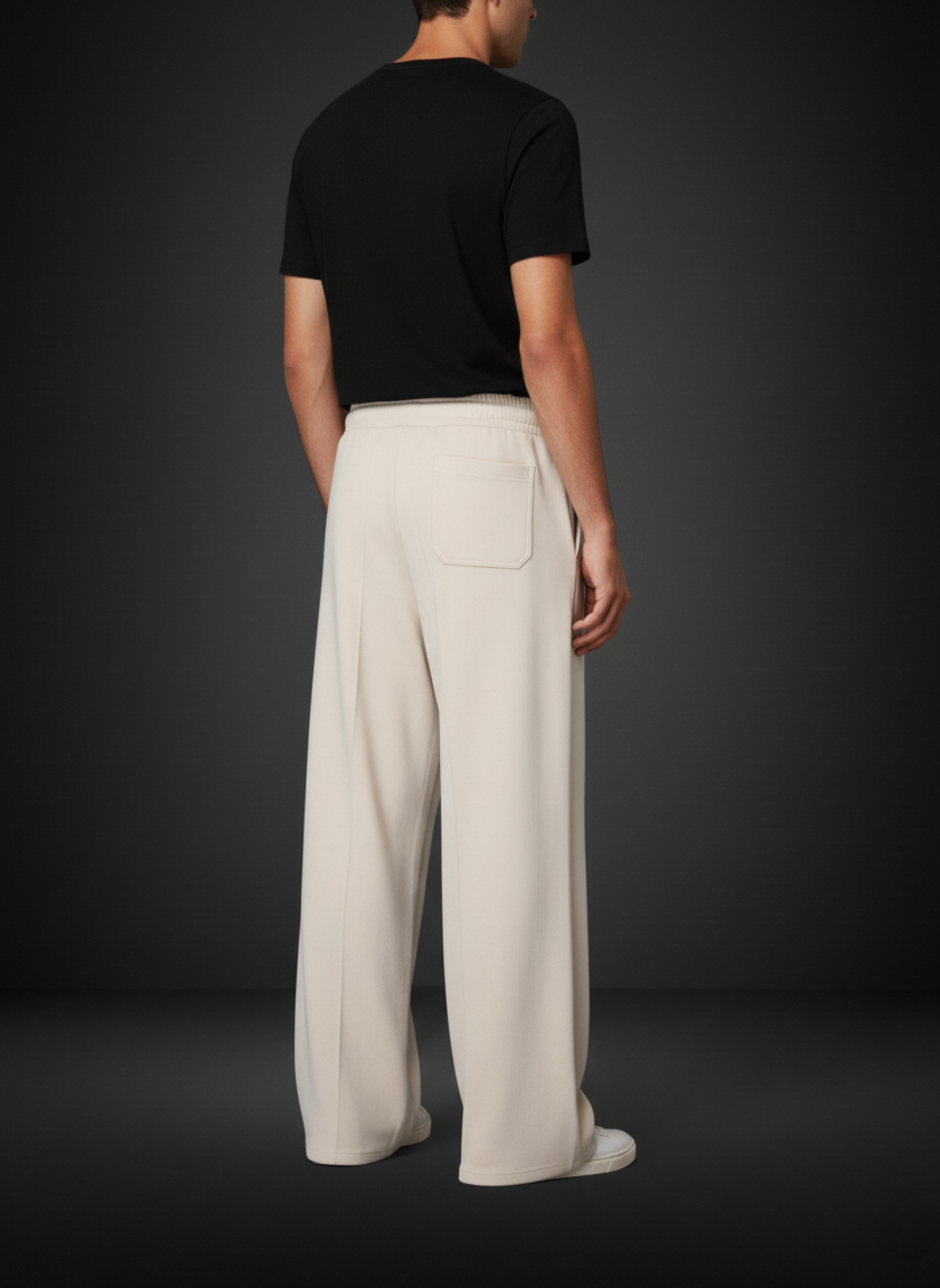 Person wearing a black t-shirt and beige pants against a dark background