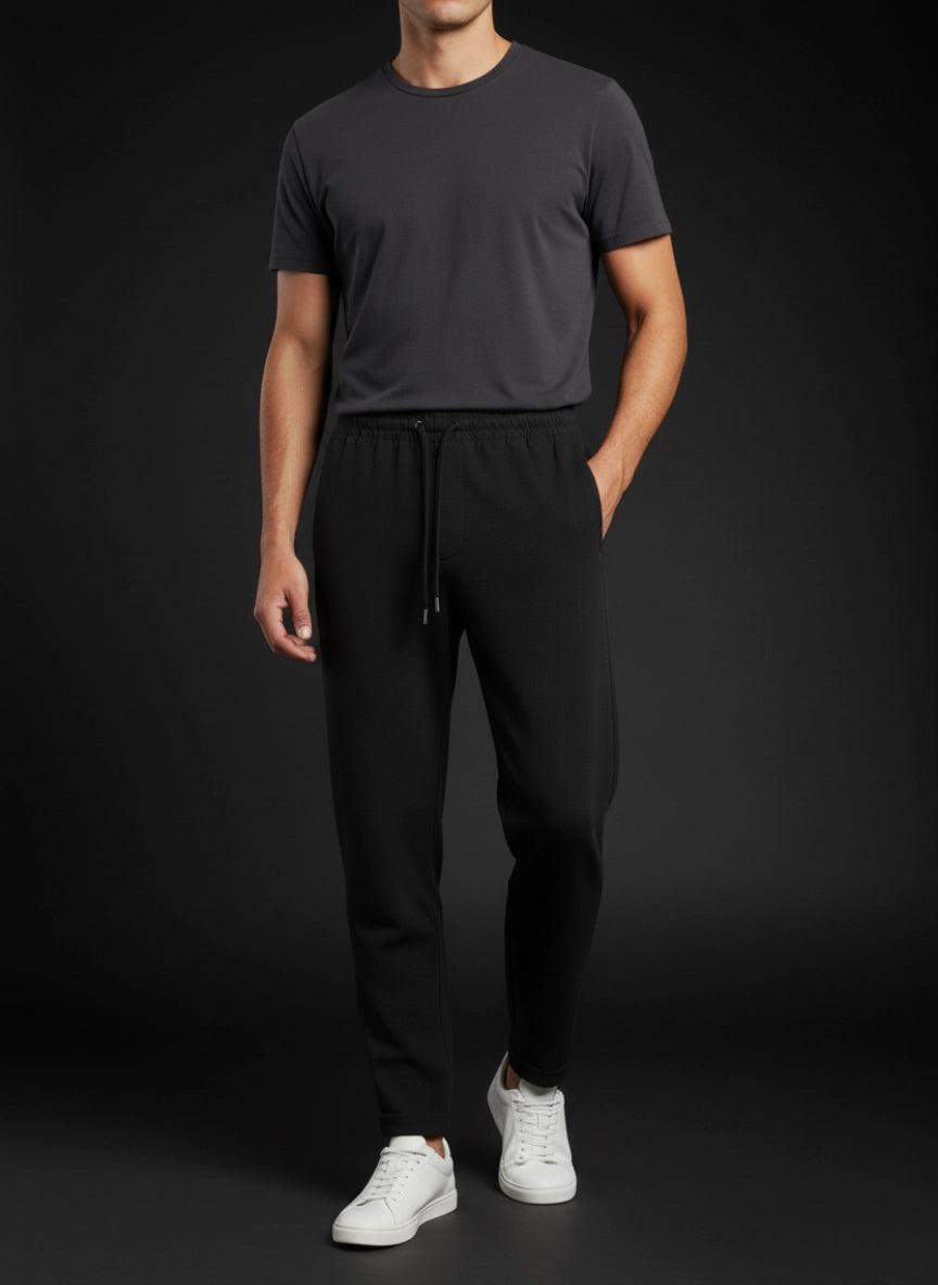 Person wearing a dark gray t-shirt and black pants with white shoes on a black background