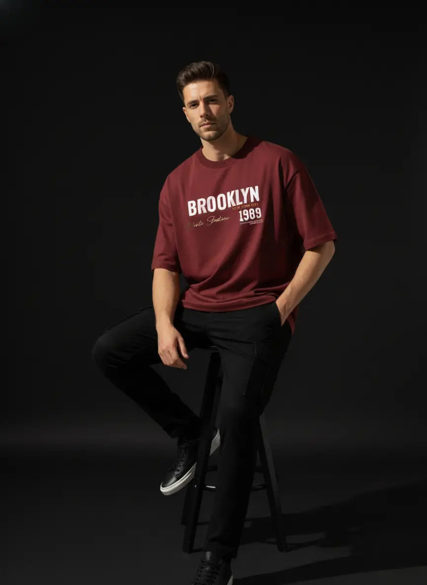 Man wearing a red t-shirt with 'Brooklyn 1969' text, sitting on a stool against a black background