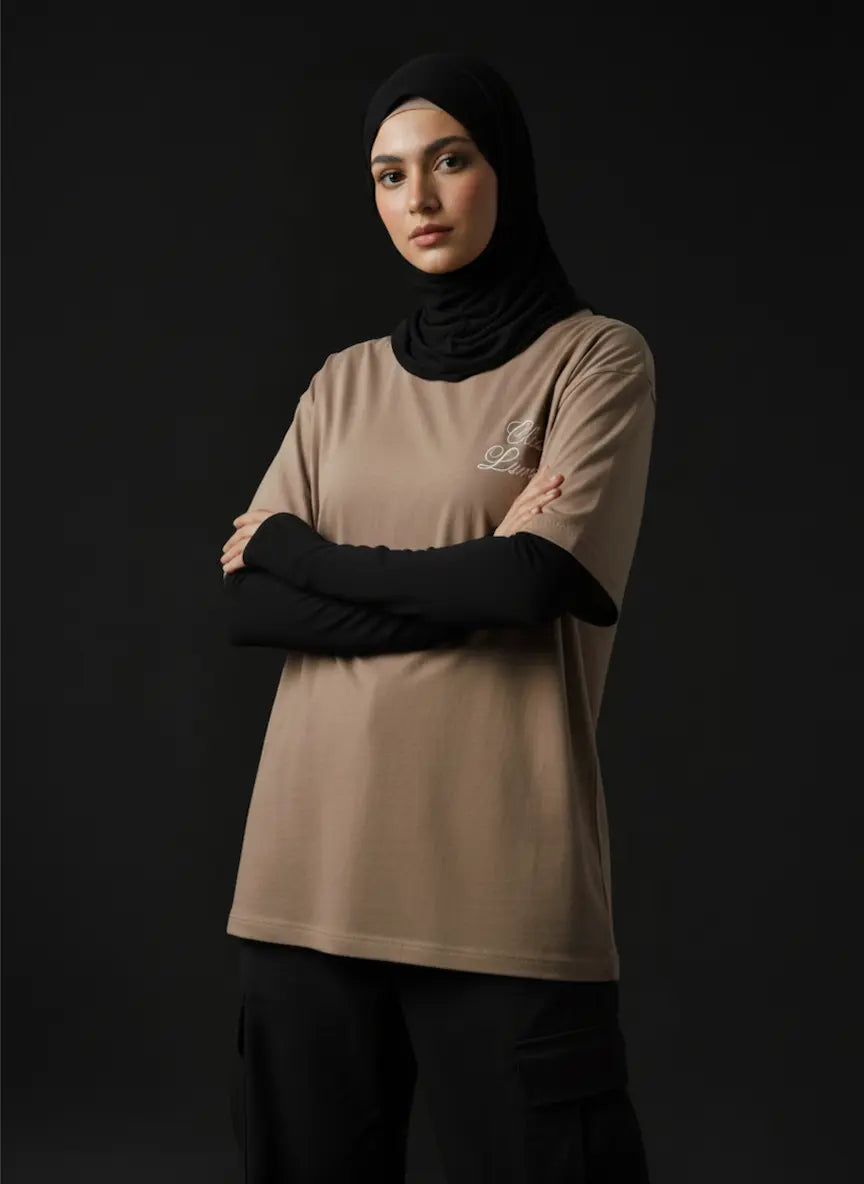 Woman wearing a beige t-shirt with a logo and black hijab on a dark background