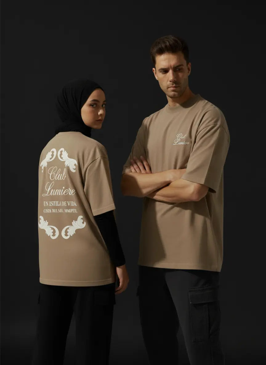 Two people wearing beige t-shirts with text and logos on a dark background