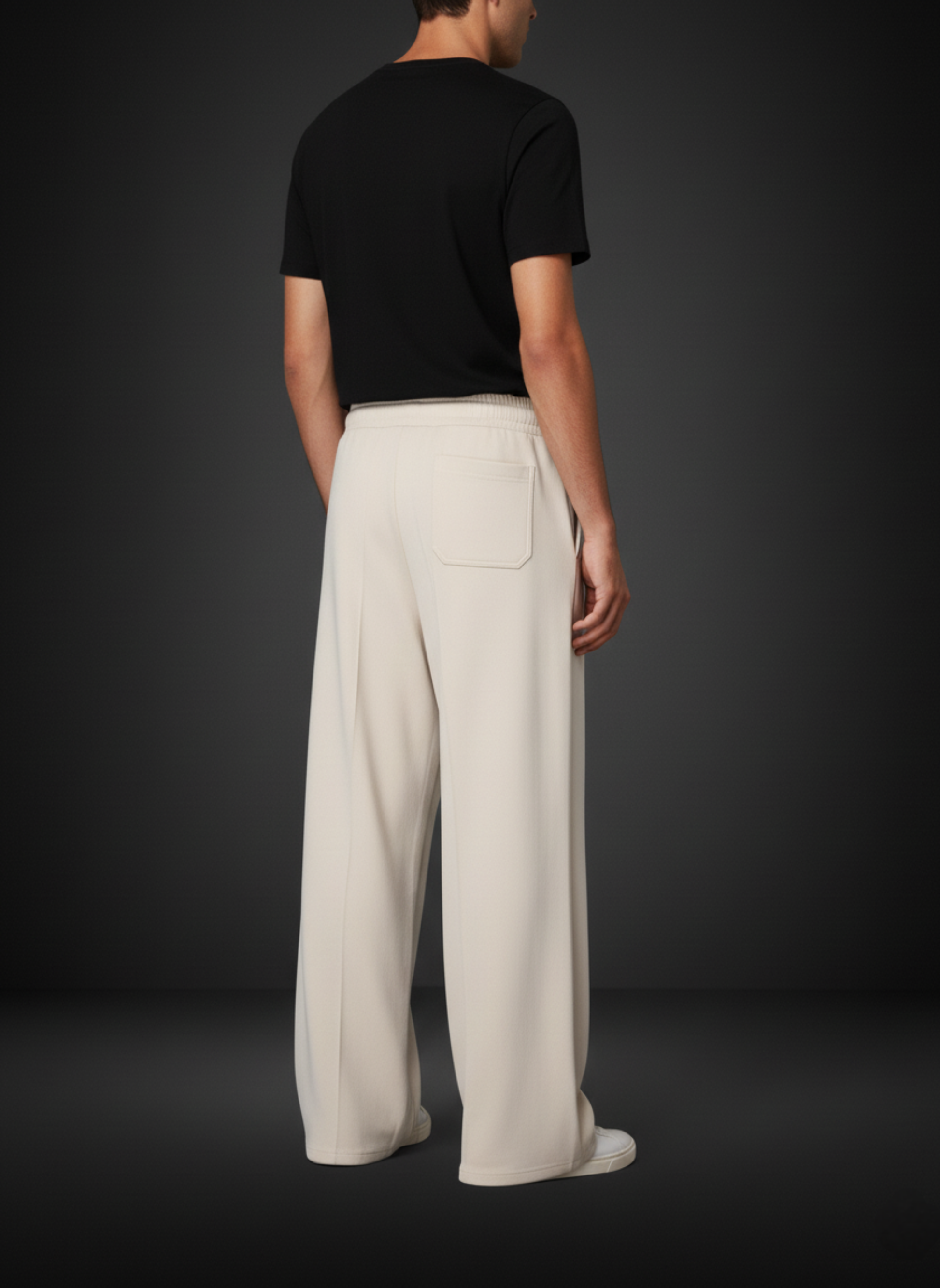 Person wearing a black t-shirt and beige pants against a dark background