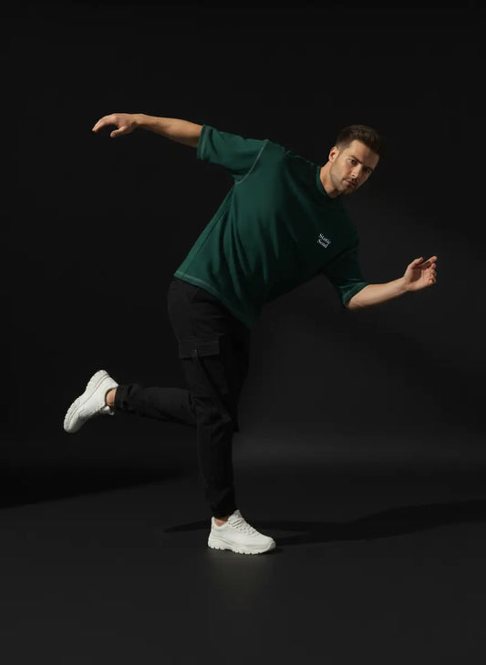 Man in green shirt and black pants posing dynamically against a black background