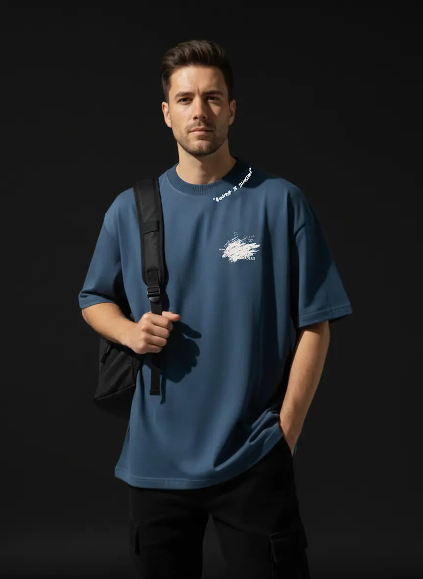Man wearing a blue t-shirt with a logo, holding a black bag against a dark background