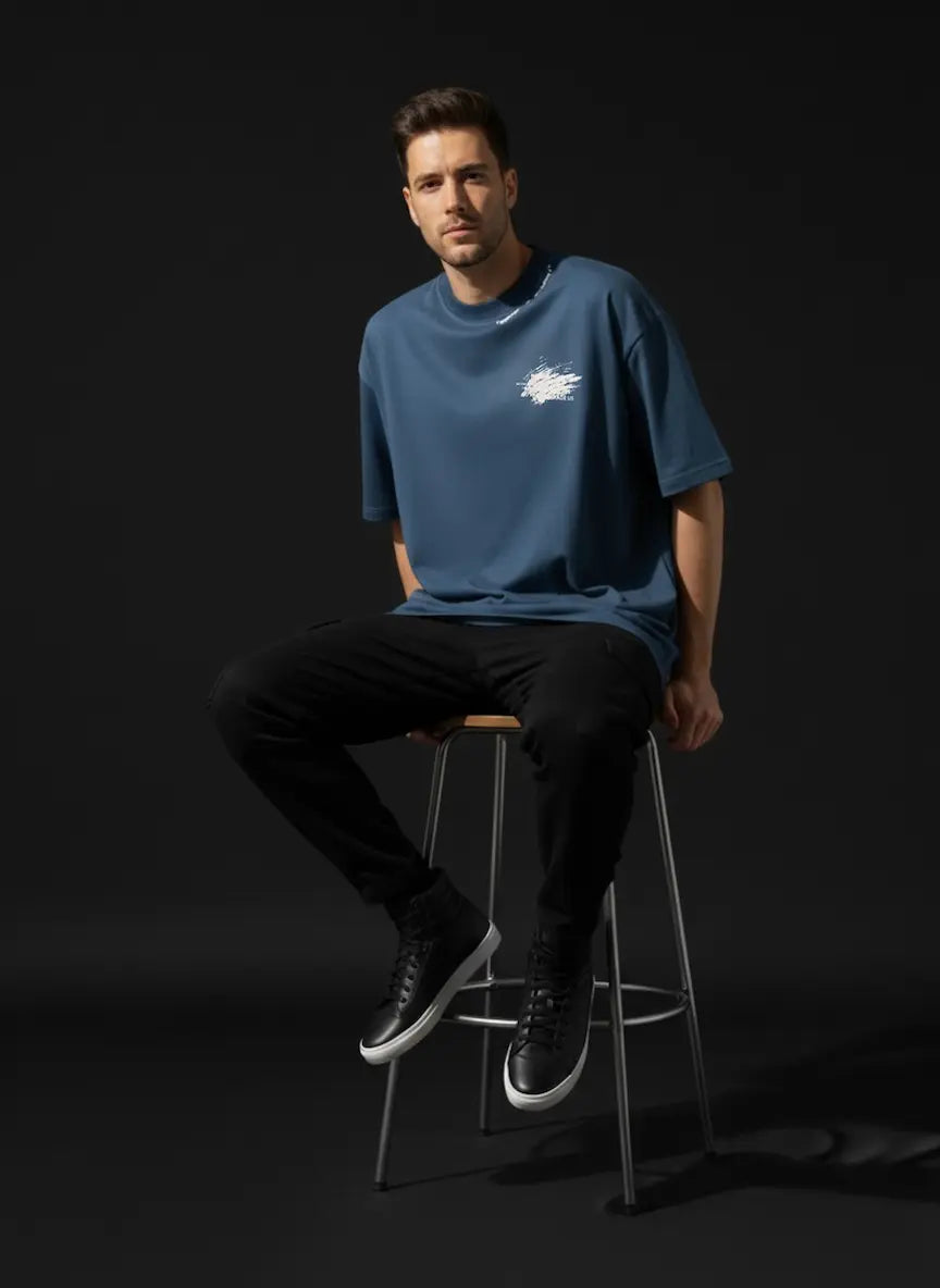 Man sitting on a stool wearing a blue t-shirt with a logo against a black background