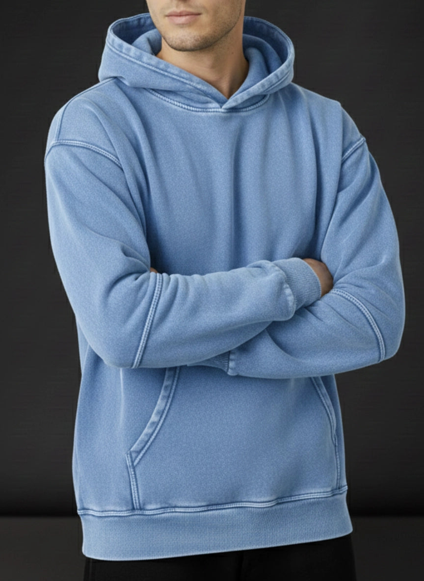 Person wearing a light blue hoodie with arms crossed on a black background