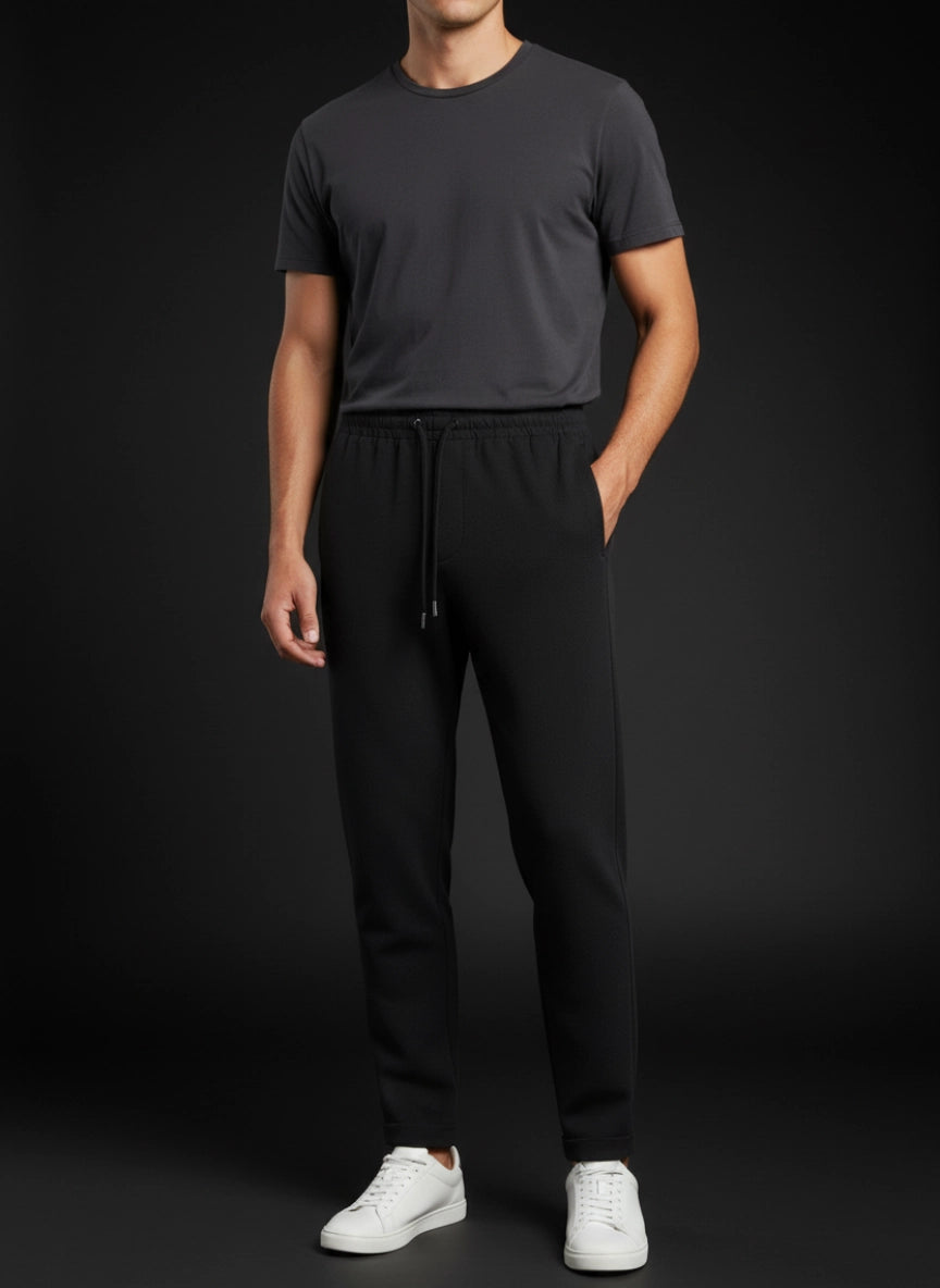 Person wearing a dark gray t-shirt and black pants with white shoes on a black background