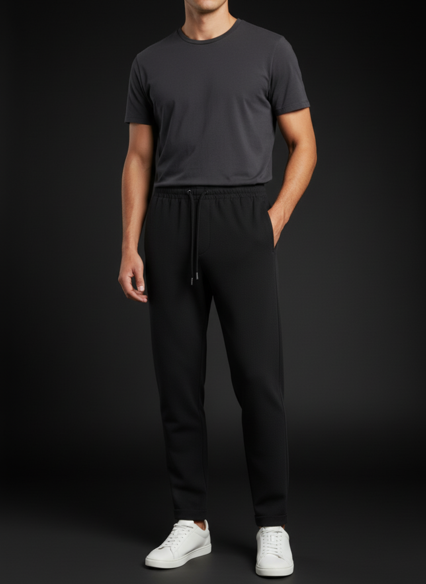 Person wearing a dark gray t-shirt and black pants with white shoes on a black background